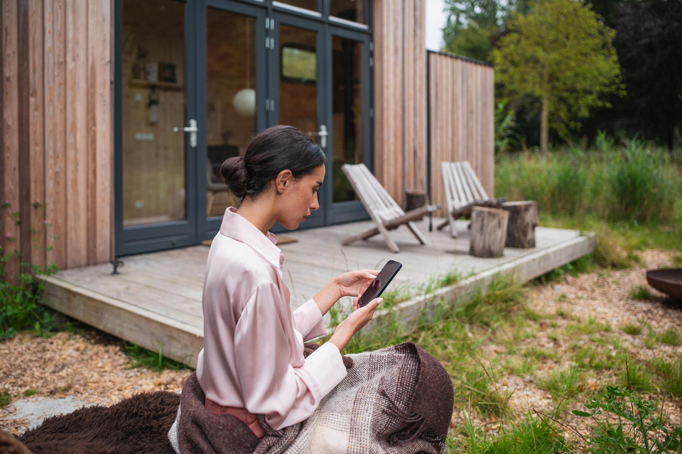 Eine Frau sitzt im Garten und schaut auf ihr Handy.