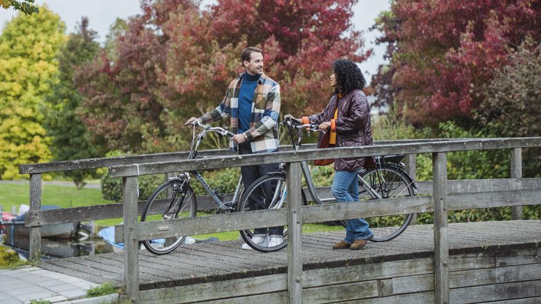 man and woman walking across bridge with bicycle in hand