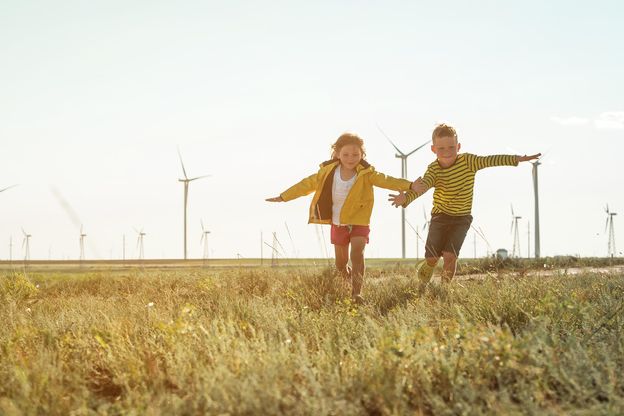 Klein meisje en jongen rennen voor windmolens. Hernieuwbare energiebronnen en duurzame hulpbronnen