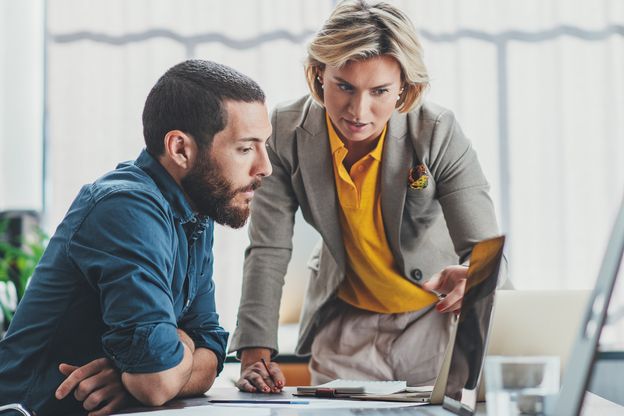 ABN AMRO Mitarbeiterin aus dem Bereich Digital Assets, mit kurzen blonden Haaren lehnt auf einem Tisch und erklärt einem Kunden die vor ihnen liegenden Analyseausdrucke.