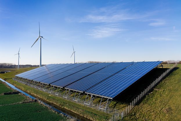 Een groen weiland vol met zonnepanelen en op de achtergrond windmolens