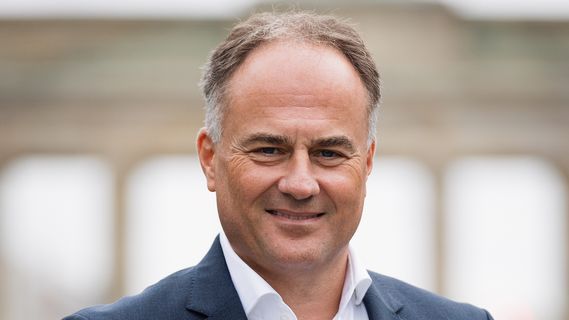 Porträt von Patrick Seitz (Direktor Bethmann HAL Berlin) in dunklem Businessanzug und weißem Hemd vor einem unscharfen städtischen Hintergrund. Im Hintergrund ist das Brandenburger Tor zu erkennen.