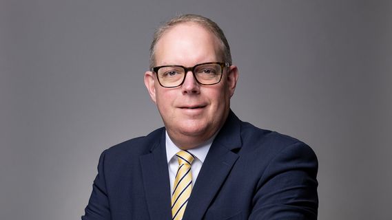 Porträt von Arndt Sauer (Niederlassungsleiter Bethmann HAL Düsseldorf) mit Brille in dunkelblauem Anzug und gestreifter Krawatte vor grauem Hintergrund. Die Person steht mit verschränkten Armen und blickt direkt in die Kamera.