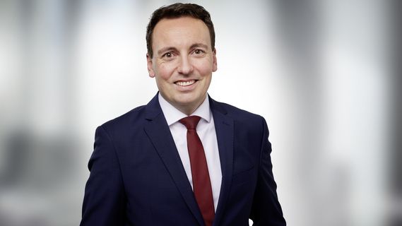 Porträt von Daniel Spanner (Niederlassungsleiter Bethmann HAL Nürnberg) in blauem Anzug, weißem Hemd und roter Krawatte vor einem hellen, unscharfen Hintergrund. Die Person blickt direkt in die Kamera und ist als Business-Porträt aufgenommen.