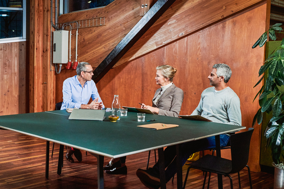 Drie personen zitten aan een groene tafel omgeven door planten