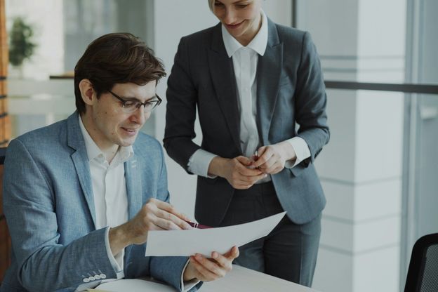 Zwei ABN AMRO Banker aus dem Bereich Financial Assets schauen sich gemeinsam einen Ausdruck an, wobei der eine Banker sitzend etwas erklärt und die Bankerin neben diesem steht und zuhört.