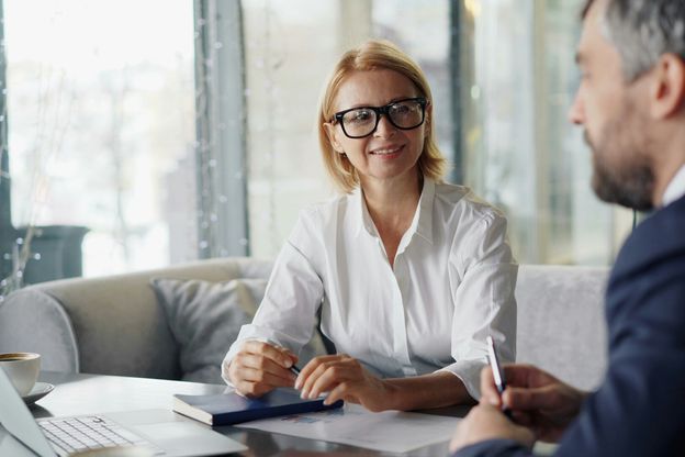 Zwei ABN AMRO Banker aus dem Bereich Asset Servicing sitzen sich gemeinsam an einem Tisch gegenüber, auf dem ein Laptop, ein Notizbuch sowie ein Statistik-Ausdruck liegt.
