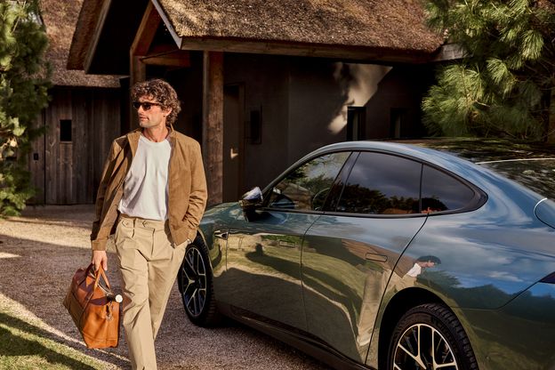 man with brown leather bag is walking in front of his car