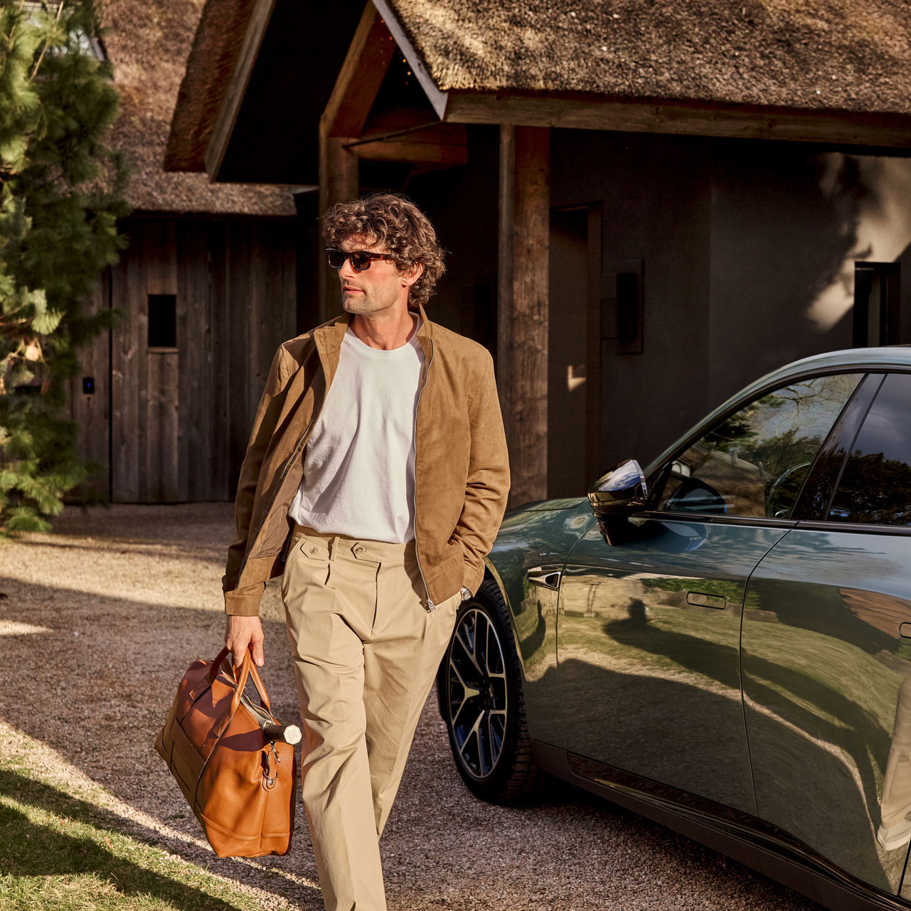 man with brown leather bag is walking in front of his car
